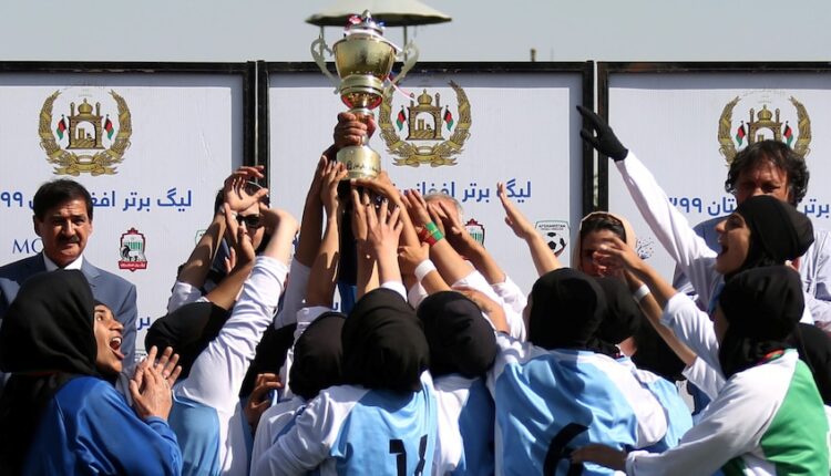 Female football players hold up a trophy.