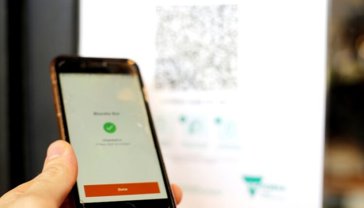 A hand holds a mobile phone with the orange Service Victoria app open to sign in with a QR code.